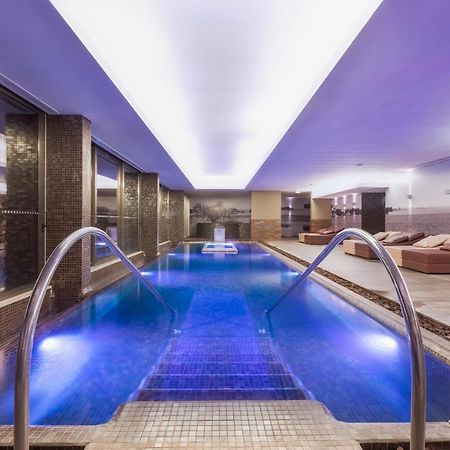 Ap Lago Montargil - Conference & Spa Εξωτερικό φωτογραφία The photo shows a modern indoor swimming pool area. The pool features a sleek design with steps leading into the water and a gentle curve at the sides. The water is illuminated in a blue hue, enhancing the relaxing atmosphere. Surrounding the pool ar