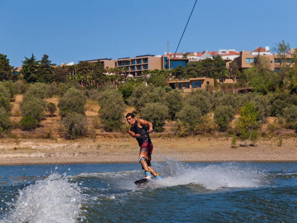 Ap Lago Montargil - Conference & Spa Εξωτερικό φωτογραφία The photo shows a person wakeboarding on a body of water. The individual is being pulled by a cable, which is likely connected to a boat or a winch. The person is wearing a life jacket and swim shorts, balancing on the board as they enjoy the activit