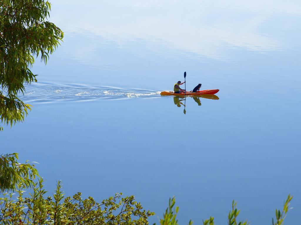 Ap Lago Montargil - Conference & Spa Εξωτερικό φωτογραφία The photo shows a serene scene of a person kayaking on a calm body of water. The surface of the water is very smooth, reflecting the surroundings, and there is a gentle wake behind the kayak indicating movement. The kayaker is wearing a life jacket a