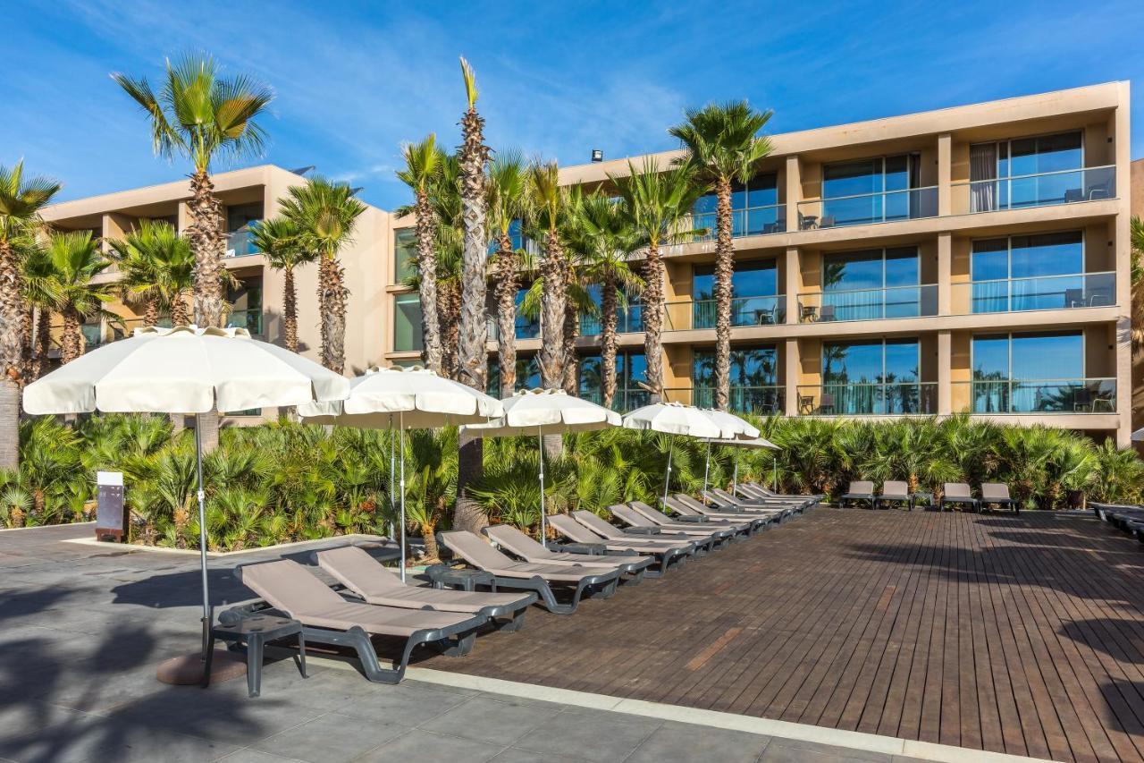 Ap Lago Montargil - Conference & Spa Εξωτερικό φωτογραφία The photo shows a modern resort or hotel area featuring several lounge chairs lined up on a wooden deck. Each lounge chair is paired with a white umbrella, providing shade. In the background, there are palm trees, which add to the tropical atmosphere