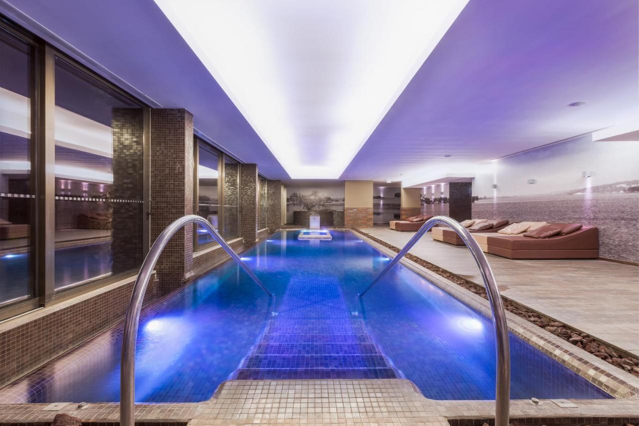 Ap Lago Montargil - Conference & Spa Εξωτερικό φωτογραφία The photo shows a modern indoor swimming pool area. The pool features a sleek design with steps leading into the water and a gentle curve at the sides. The water is illuminated in a blue hue, enhancing the relaxing atmosphere. Surrounding the pool ar