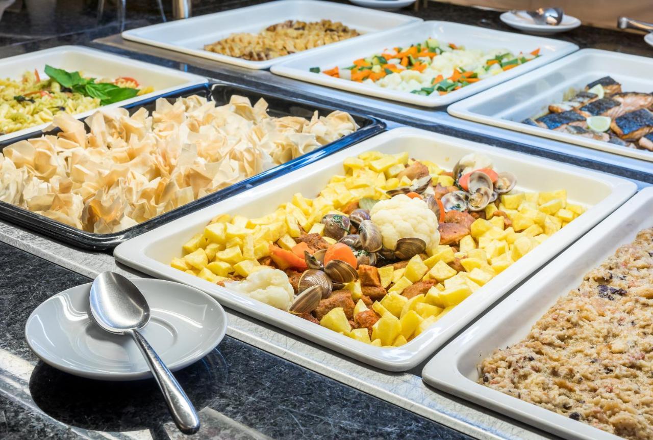 Ap Lago Montargil - Conference & Spa Εξωτερικό φωτογραφία The photo shows a buffet-style display of various dishes. There are several rectangular trays filled with different types of food. 

1. One tray contains a mix of vegetables and seafood, likely including potatoes and cauliflower.
2. Another tray hold