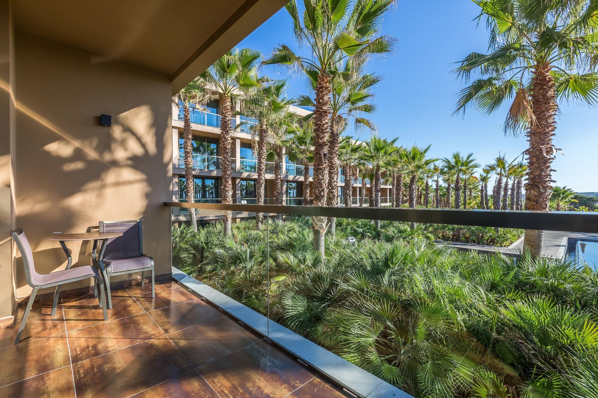 Ap Lago Montargil - Conference & Spa Εξωτερικό φωτογραφία The photo shows a balcony with modern furniture, including a chair and a small table. In the background, there are tall palm trees and lush greenery, suggesting a tropical or resort-like setting. The buildings in the distance are likely part of a hot