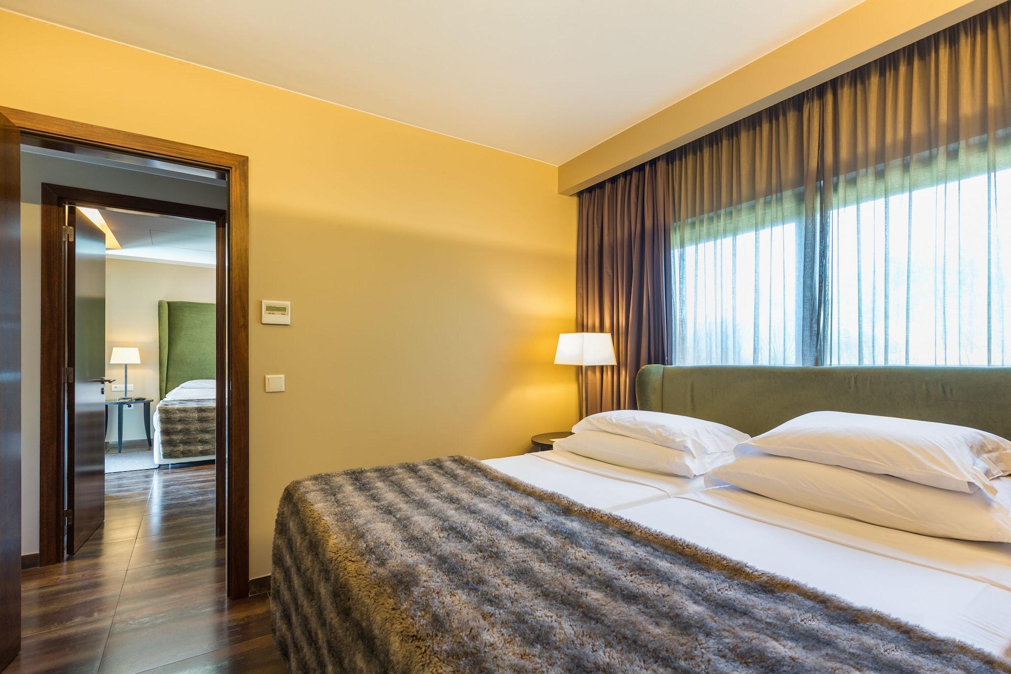 Ap Lago Montargil - Conference & Spa Εξωτερικό φωτογραφία The photo shows the interior of a well-furnished hotel room. It features two beds with white linens and a gray decorative throw on top. The walls are painted a warm yellow, and there are floor-to-ceiling windows covered with dark curtains that allow 