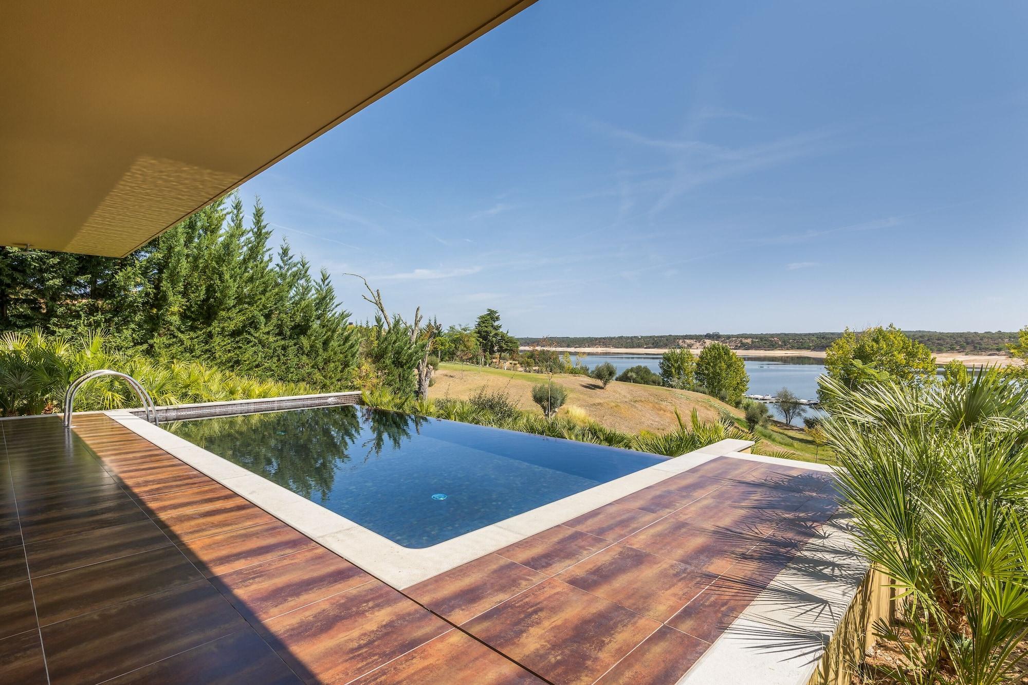 Ap Lago Montargil - Conference & Spa Εξωτερικό φωτογραφία The photo shows a luxurious infinity pool situated on a terrace or deck. The pool features a sleek, modern design with a dark blue surface that reflects the surrounding scenery. In the background, there is a landscape of rolling hills and a body of w