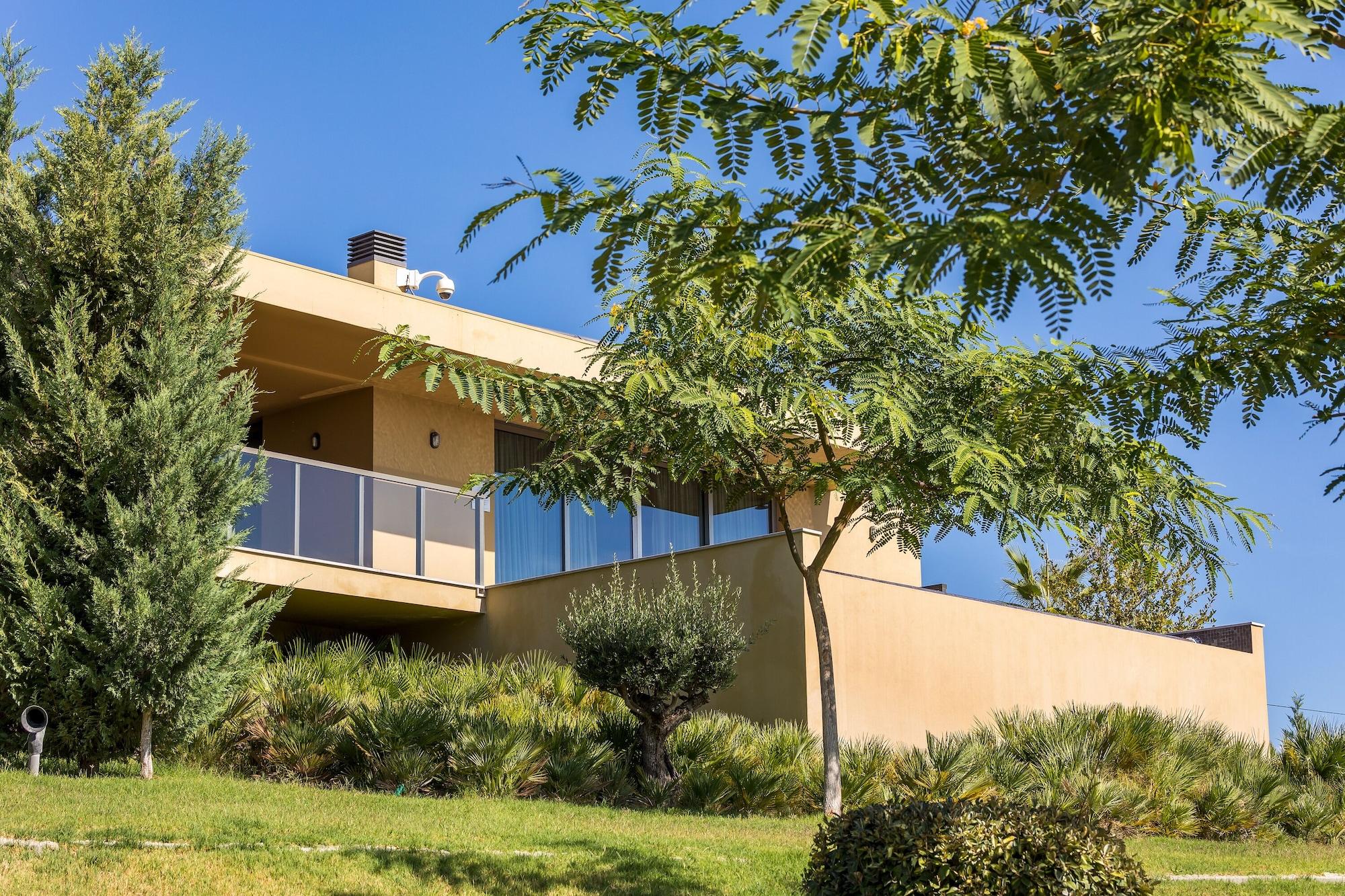 Ap Lago Montargil - Conference & Spa Εξωτερικό φωτογραφία The photo showcases a modern house situated on a grassy slope. The house features a light-colored exterior with large windows and a balcony. Surrounding the building are several trees and landscaping that enhances the natural environment. The sky is 