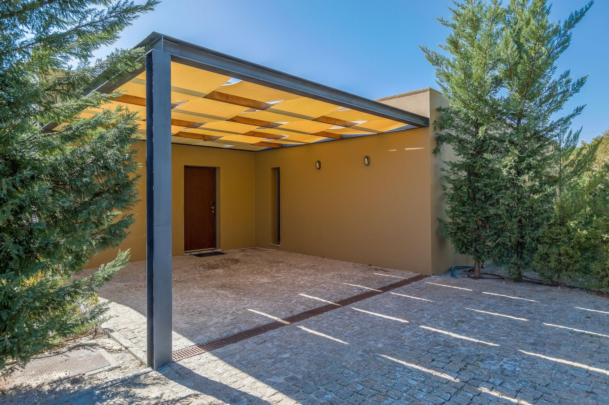 Ap Lago Montargil - Conference & Spa Εξωτερικό φωτογραφία The photo shows an exterior view of a modern structure with a carport. The carport has a sleek, metallic frame and a yellowish canopy above it. In front of the structure, there is a paved area made of stone or tiles. The main entrance features a wood