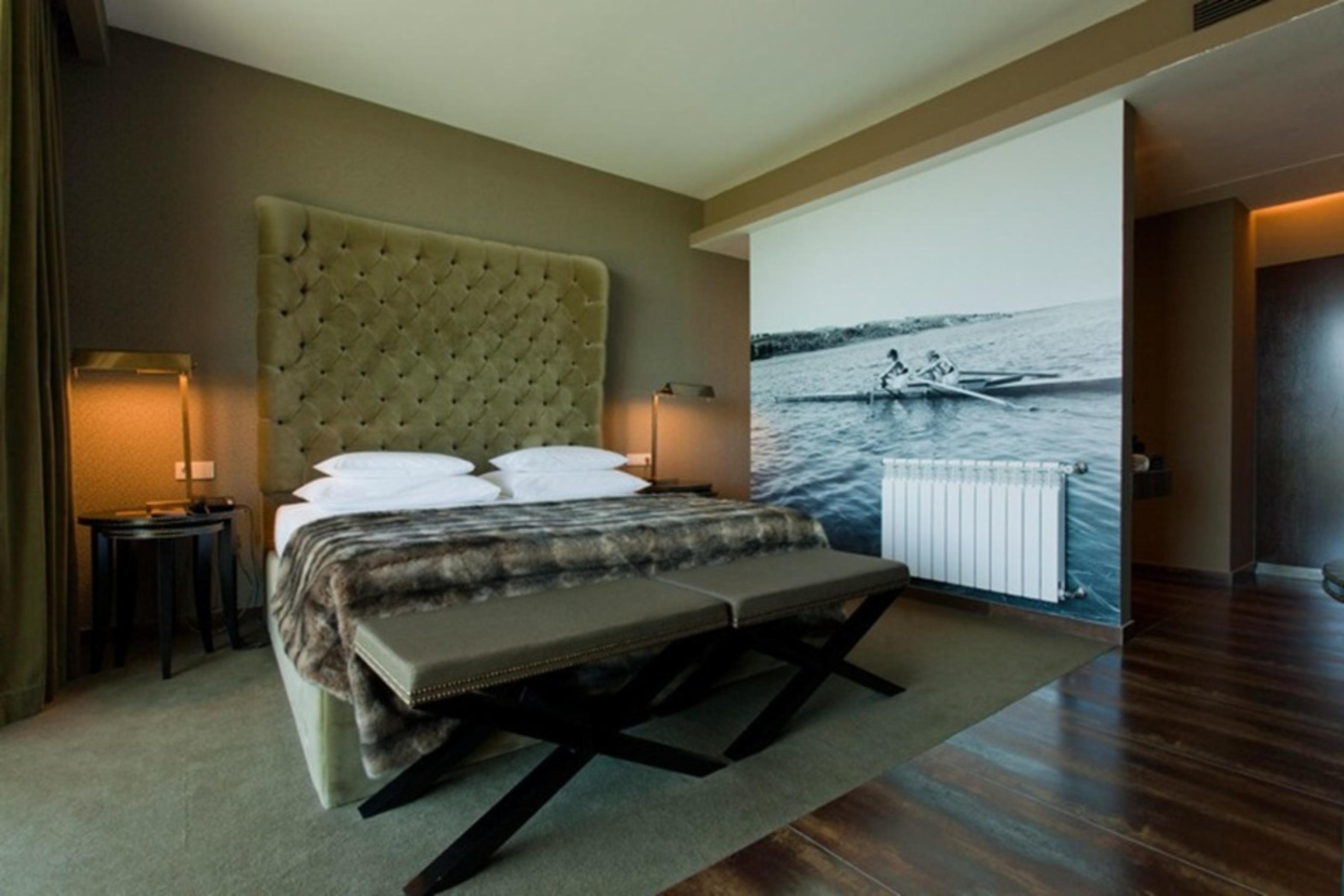 Ap Lago Montargil - Conference & Spa Εξωτερικό φωτογραφία The photo shows a modern hotel room featuring a large bed with a tufted headboard and plush bedding. The color palette is neutral, with shades of green and gray. On one side of the room, there are bedside tables with lamps. A comfortable bench sits a
