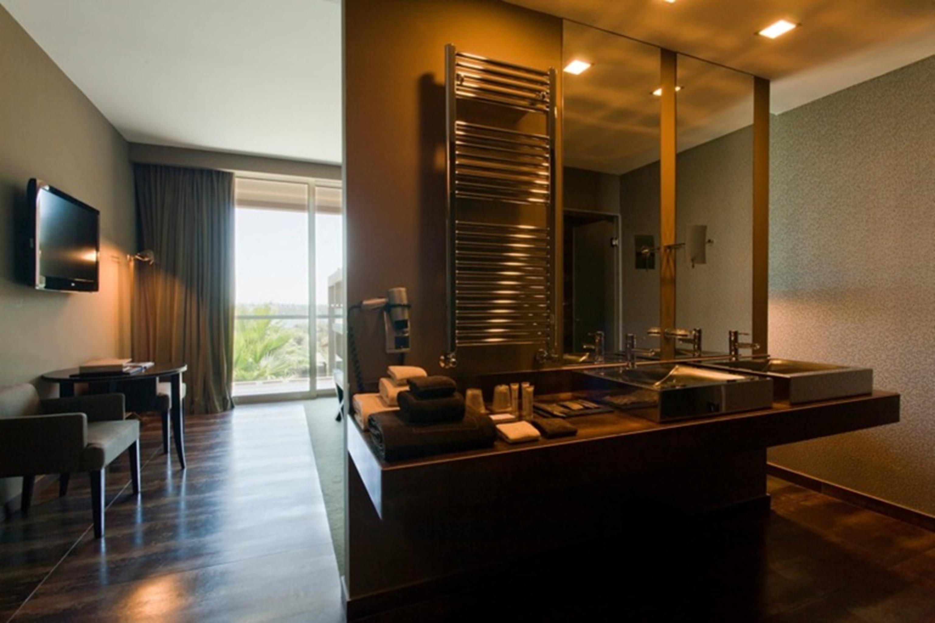 Ap Lago Montargil - Conference & Spa Εξωτερικό φωτογραφία The photo displays a modern hotel room with a contemporary design. The room features a large window, allowing natural light to enter and offering a view outside. On one side, there is a sitting area with a small table and chairs. The other side showc