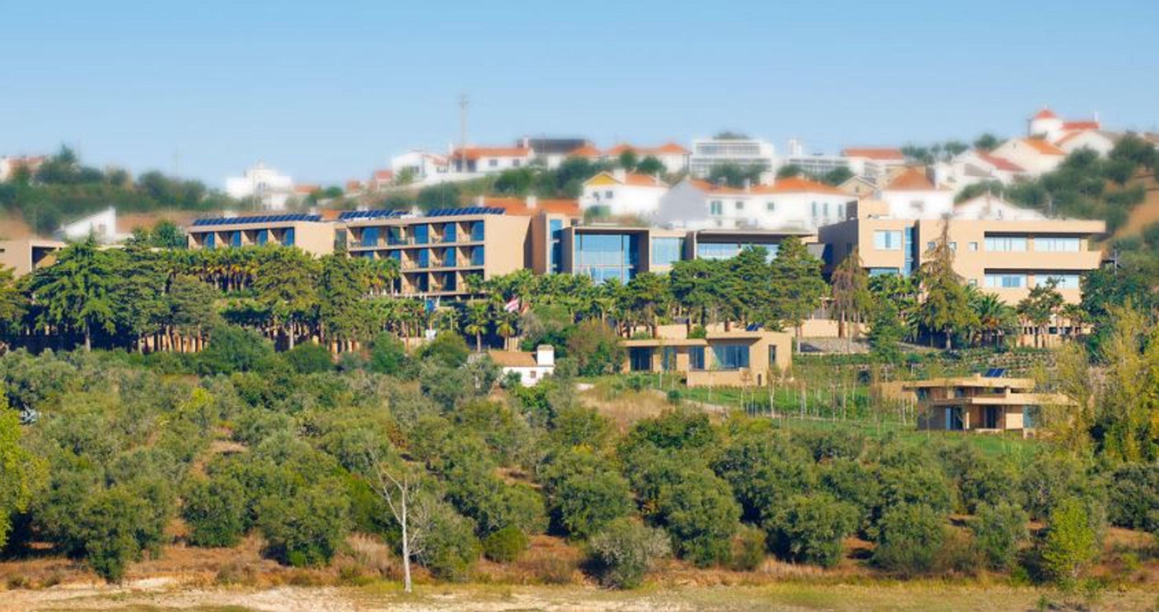 Ap Lago Montargil - Conference & Spa Εξωτερικό φωτογραφία The photo shows a hillside view of a modern resort or hotel complex surrounded by greenery. The buildings are designed with a blend of contemporary architecture and natural elements, featuring wooden accents, large windows, and terraces. In the backg