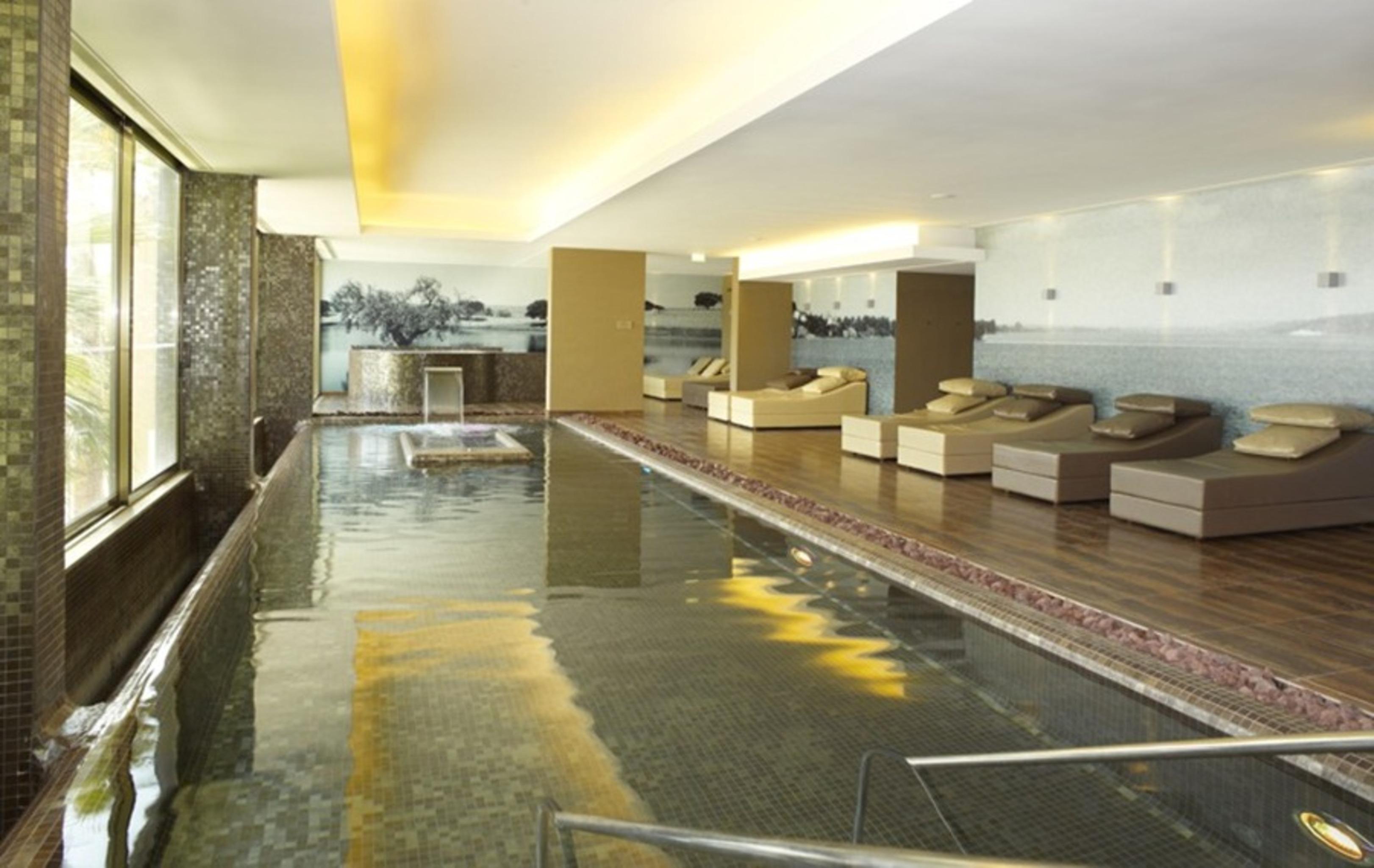 Ap Lago Montargil - Conference & Spa Εξωτερικό φωτογραφία The photo shows a modern, serene spa environment. There is a swimming pool with calm water, reflecting the surrounding decor. Along the sides, there are several comfortable lounge chairs arranged, perfect for relaxation. Large windows allow natural l