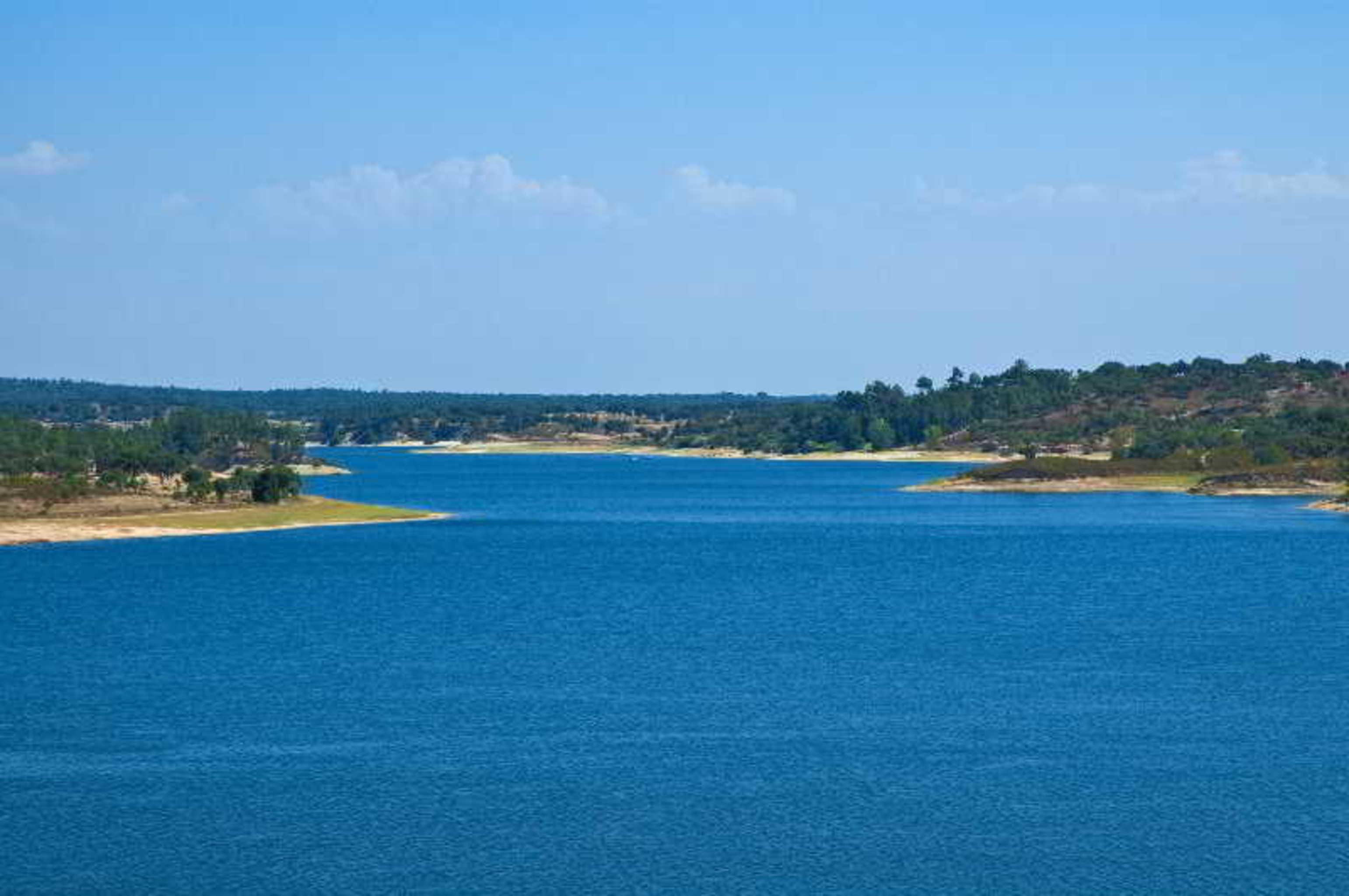 Ap Lago Montargil - Conference & Spa Εξωτερικό φωτογραφία The photo depicts a serene landscape featuring a large body of water, likely a lake or river. The water appears calm and is reflecting a clear blue sky with some clouds. Surrounding the water, there are patches of green land and trees, indicating a n