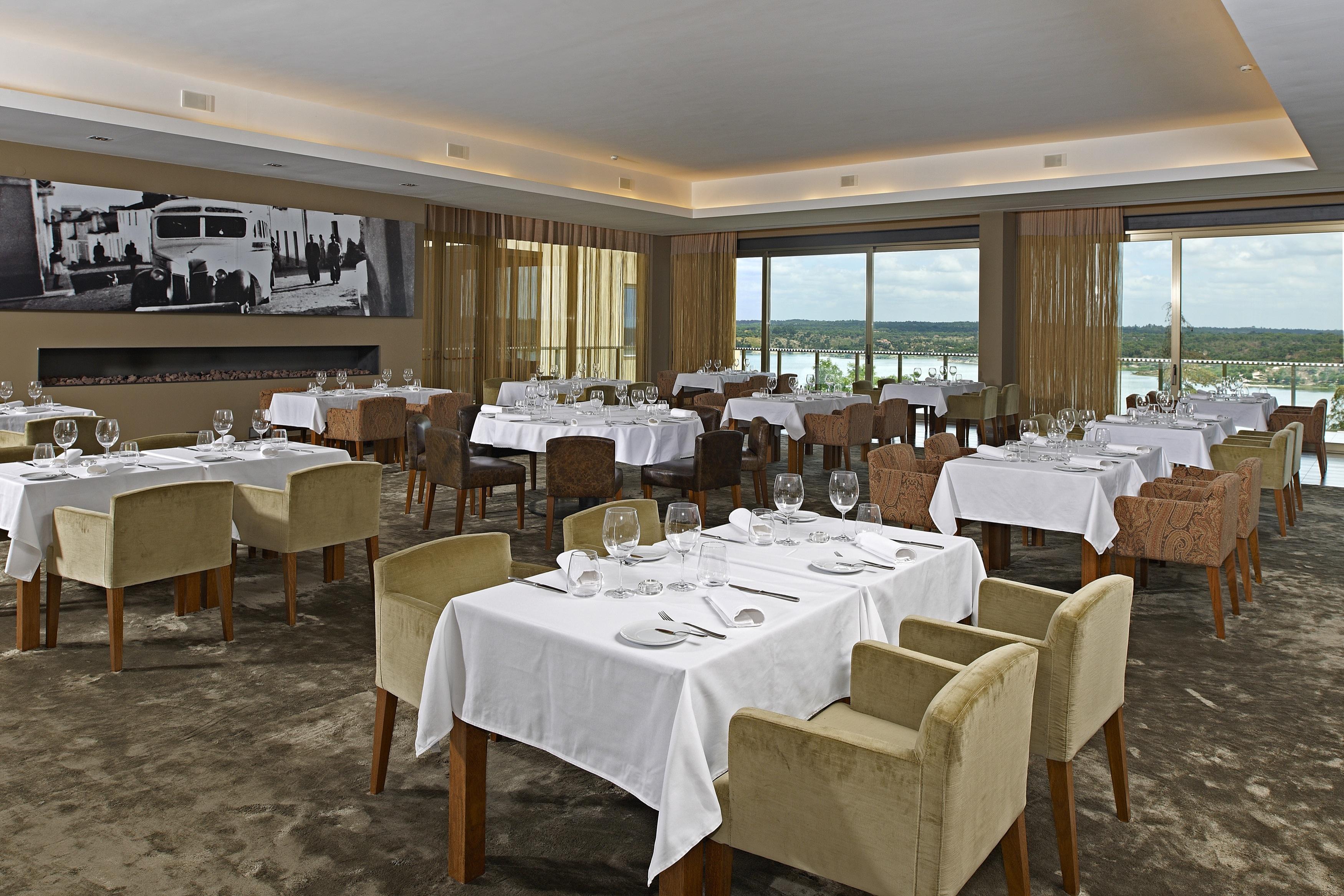 Ap Lago Montargil - Conference & Spa Εξωτερικό φωτογραφία The photo shows an elegant restaurant interior featuring neatly arranged tables with white tablecloths. Each table is set with plates, cutlery, and glasses. The seating includes a mix of upholstered chairs in different colors—some light and others da