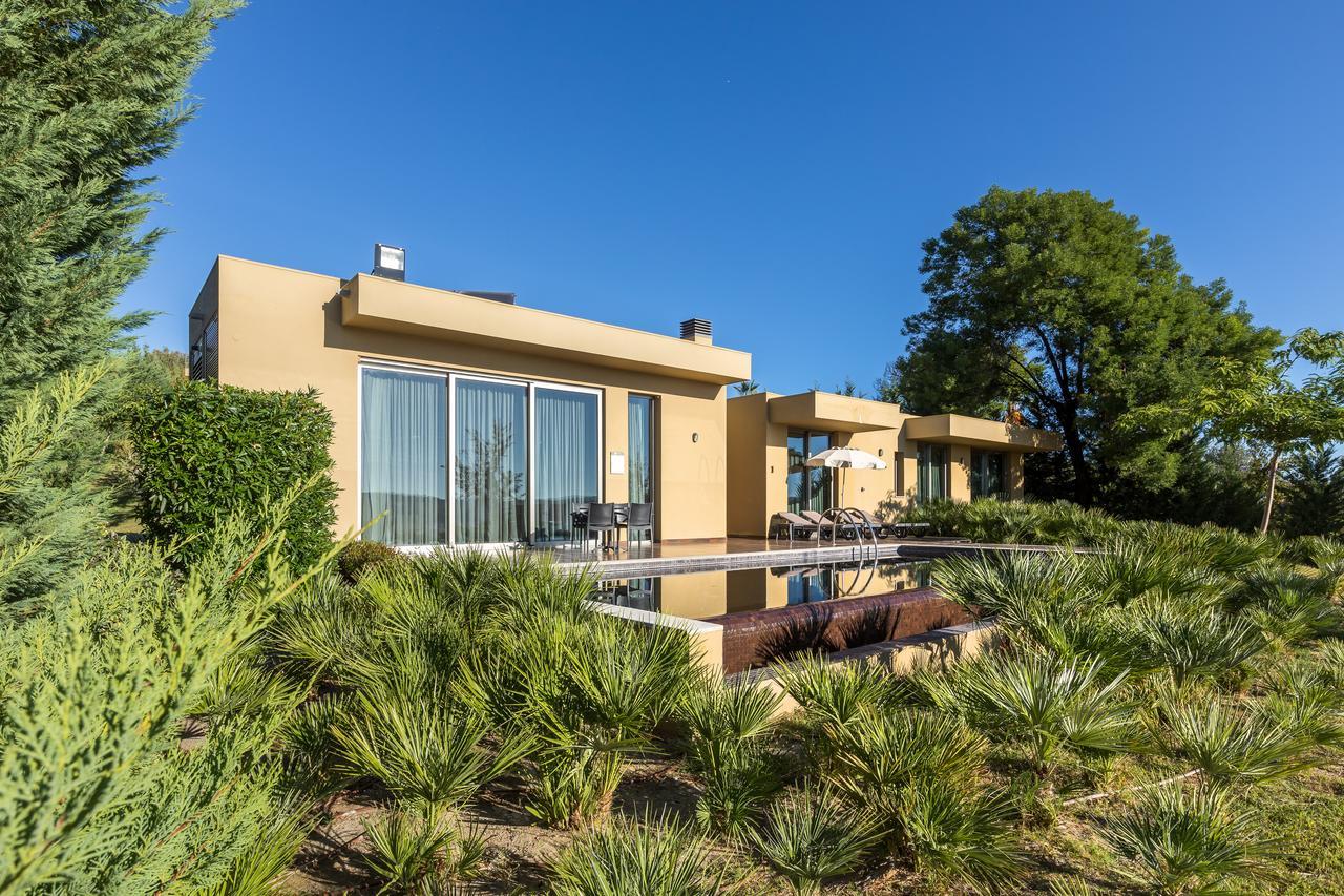Ap Lago Montargil - Conference & Spa Εξωτερικό φωτογραφία The photo shows a modern villa or house set in a natural landscape. The building features a contemporary design with large glass windows and a beige exterior. In front of the house, there is a pool area, and the surrounding landscape includes greener