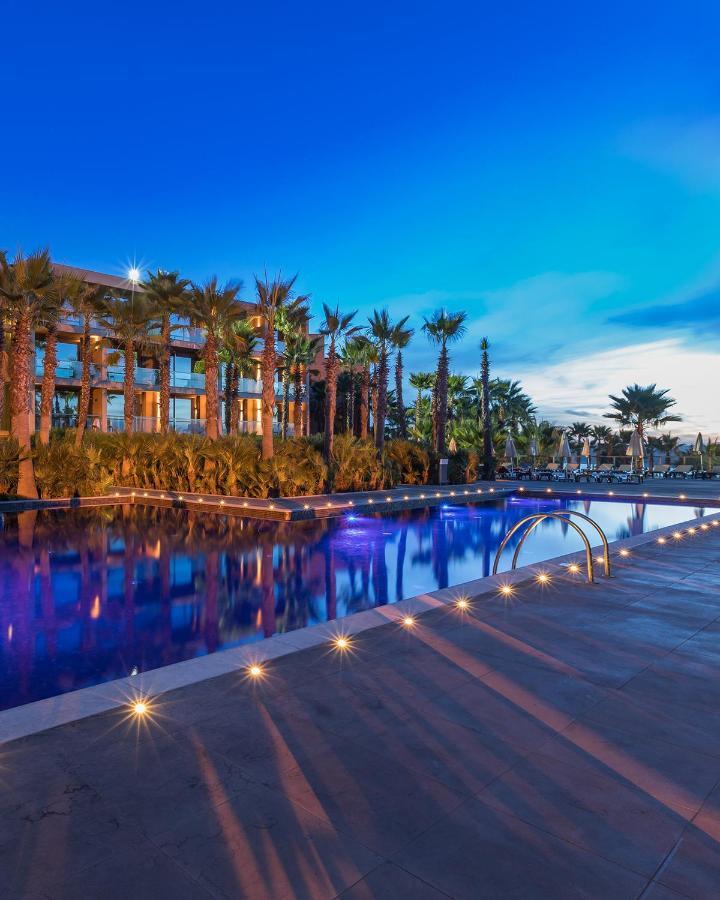 Ap Lago Montargil - Conference & Spa Εξωτερικό φωτογραφία The image shows a serene and inviting outdoor area with a large swimming pool that features a beautiful blue hue, likely illuminated by lights. Surrounding the pool are well-maintained palm trees and lush greenery, creating a tropical atmosphere. In 